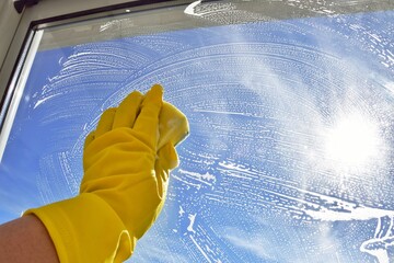 A woman washes a window.  Household chores
