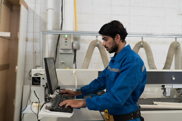 Plywood processing plant. Furniture manufacturing. Operator use desktop computer control CNC...