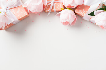 Pink peonies and gift boxes with white ribbons from a top border on a white background. Ideal for festive occasions, greetings, and invitations with copy space.