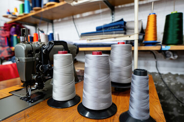 Sewing workshop with industrial machine and large spools of thread on wooden table