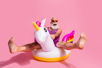 Elderly man enjoying summer holidays on inflatable unicorn against pink background