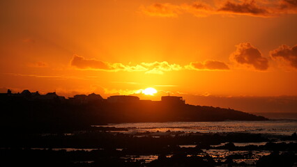 Scenic sunset over ocean with silhouette of coastline and glowing orange sky, tranquil seascape and nature background
