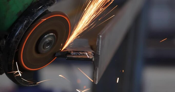 Steel worker grinding a metal construction with grinder in the factory, close up slow motion
