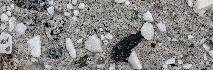 Concrete wall texture with pebbles. Decorative rough concrete surface with white, black and gray stones. Wide panoramic texture for background and design.