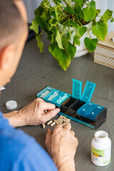 Man sorting his pills and supplements into a weekly pill organizer. Concept of medication management and daily health routine