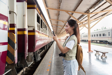 Obraz premium Travel Enthusiasm and Smartphone Use. A joyful woman taking a selfie at the train station, capturing her travel moments.