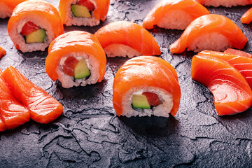 Salmon uramaki sushi roll, sashimi slices, and nigiri on a black stone background
