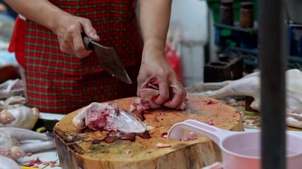 A butcher is cutting chicken meat using a knife at a traditional market