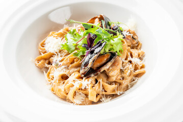 A delectable pasta dish featuring tagliatelle tossed in a creamy sauce, topped with fresh mussels, grated cheese, and garnished with mixed greens. Perfect for seafood lovers.
