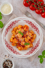Traditional potato gnocchi with tomato sauce, parmesan cheese and fresh basil on a plate on a concrete background. Italian cuisine. Top view, copy space.