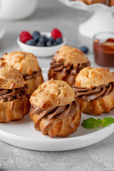 Profiteroles with chocolate cream, fresh berries and chocolate glazed on a plate on a gray concrete background. A delicious French dessert.
