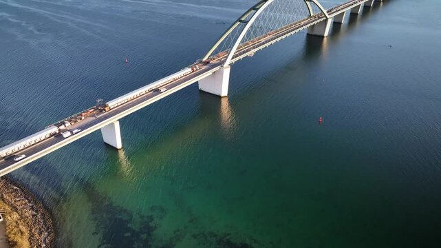 Aerial footage capturing vehicles traveling along the Fehmarn Sound Bridge, the arch bridge connecting mainland Germany with Fehmarn Island. Tilt up view of the bridge over Baltic Sea.