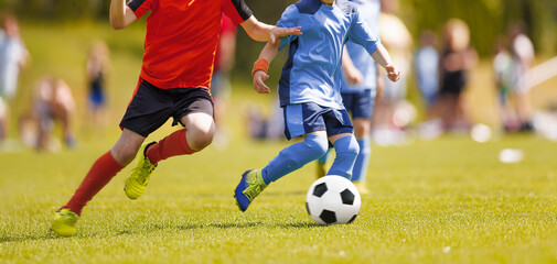 Kids Football Players Kicking Ball on Soccer Field. Sports Soccer Horizontal Background. Spectators on Stadium in the Background. Youth Junior Athletes in Red and Blue Soccer Shirts. Sports Education © matimix
