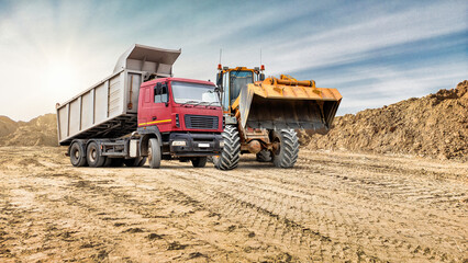 Fototapeta premium Heavy machinery at a construction site during golden hour with a truck and a loader preparing for work