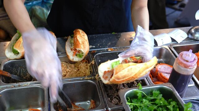 Female chef serving traditional vietnamese sandwich Banh Mi in street food with meats, pork roll and vegetables. It combines Vietnamese cuisine with French condiments like pate