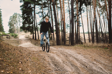 Obraz premium A young person rides a bicycle on a dirt path through a forest, suggesting outdoor activity and adventure.