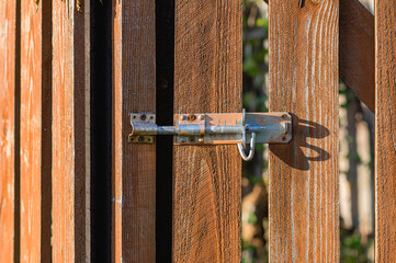 Metal latch on a wooden gate in sunlight. Close up.