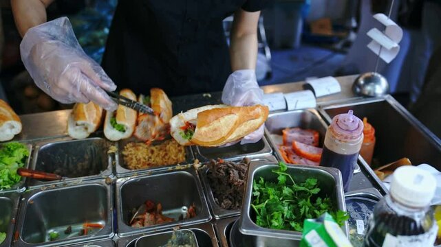 Female chef serving traditional vietnamese sandwich Banh Mi in street food with meats, pork roll and vegetables. It combines Vietnamese cuisine with French condiments like pate