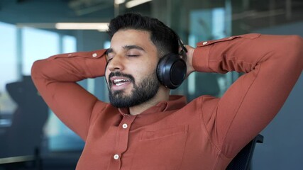 Happy businessman in wireless headphones listening to relaxing music with eyes closed during break at work sitting in office. Satisfied man relaxes to sounds of relaxation and noise of nature Close up - Powered by Adobe