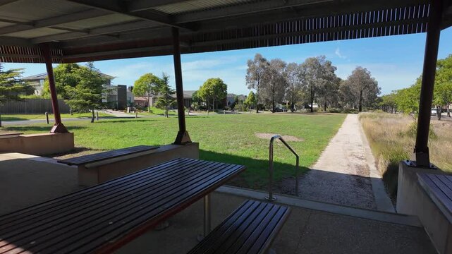 Covered public picnic shelter with fixed benches and table in Williams Landing,Melbourne Australia. The shelter provides a shaded rest area overlooking suburban neighborhood with rows of modern houses