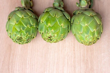 Three vibrant green artichokes are aligned against a natural woodgrain surface, showcasing their...