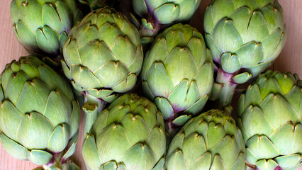 Fototapeta premium A detailed view of multiple green artichokes laid out on a table showcasing their texture. The image highlights the fresh, natural appearance of these vegetables, ideal for culinary, food, diet