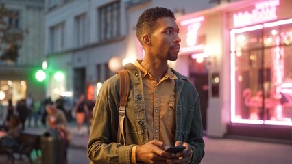 Low angle view portrait of beautiful man standing on street texting online with smartphone. Focused...