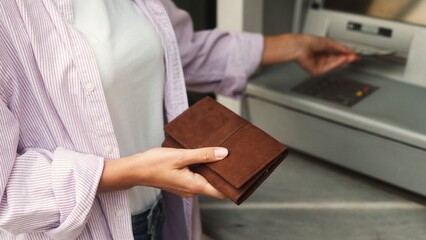 Extreme close-up view of young woman withdrawing money counting euro bills putting in wallet. Caucasian female standing in front of ATM terminal cashing out credit card. Finance concept.