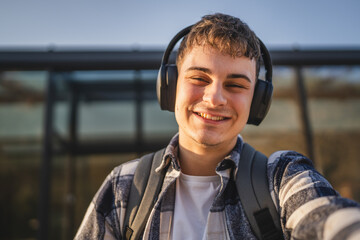 young man with headphones and backpack in front modern building