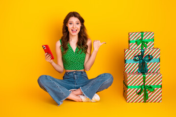 Joyful young woman with a phone gesturing towards gift boxes, expressing happiness and excitement...