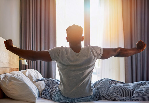 Happy man stretching in bed after waking up from sleep at home in the morning. She enjoys the pleasant start to day, appreciating the morning light and feeling refreshed and energized