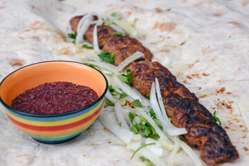 Kebab with onion and pita bread on a wooden table. Shish kebab with ketchup, herbs. Grilled kebab wrapped in pita bread. Restaurant food. Fast food with meat barbecue