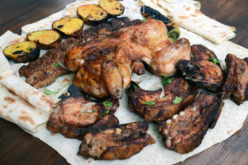 Grilled chicken with potatoes and pork barbecue on the table. Pork and chicken barbecue wrapped in pita bread. Roasted chicken and meat bbq