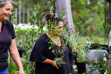 Happy female gardener with nursery garden customer holding potted plants to buy