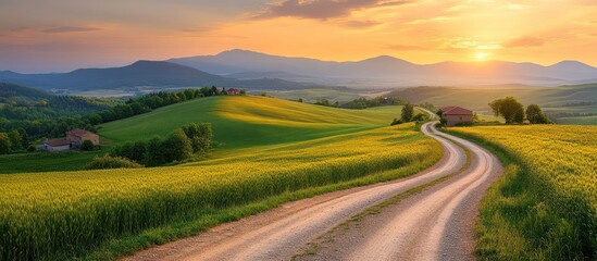 Sunset rural road winding through yellow fields, houses, mountains background