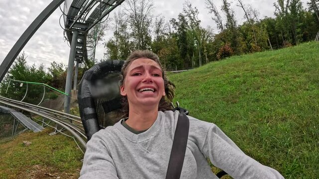 Thrilled woman enjoying ride alpine coaster through scenic forested hillside, captured with front-facing camera Woman Riding Mountain Coaster with Excited Expression woman enjoying ride alpine coaster