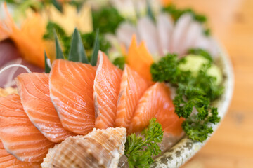 Freshly sliced salmon sashimi arranged on ice in a ceramic bowl, garnished with parsley and seashells for decoration.