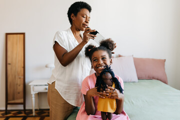 Black mother combing and caring for her daughter's hair in the bedroom