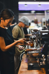 Shot in low light of female barista making a fresh coffee in cafe.