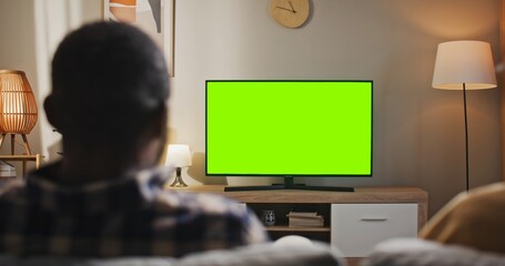 African American man sitting at couch. Male relaxing at home watching chroma key screen. Man...