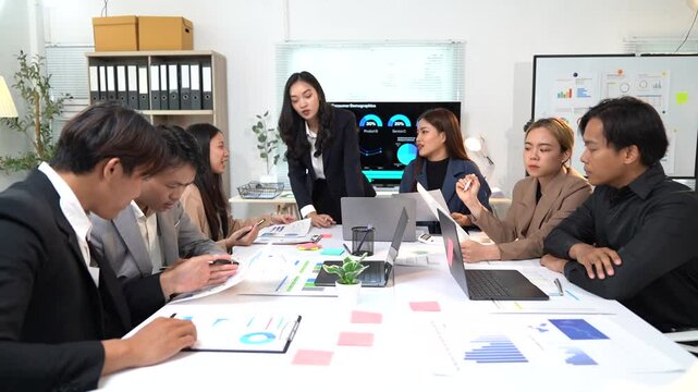 Professional Asian business team collaborating during strategic meeting, reviewing financial graphs, analyzing data, planning project development with shared vision and collaborative approach