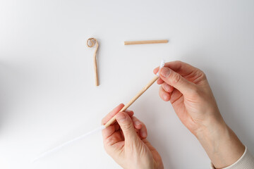 a step in a crafting process. It shows a pair of hands holding a paper pipe or straw with a white...
