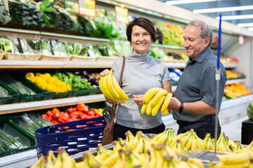 Happy cheerful man and woman choosing bananas in the store