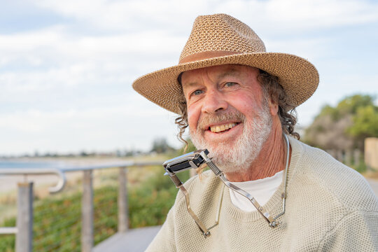 Close up of a busker wearing a hat and a harmonica around his neck smiling