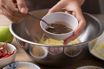 Spicy mango salad cooking, Hand adding fermented fish in bowl and mixing with ingredients