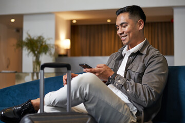 Smiling Traveler Relaxing in a Hotel Lobby Using Smartphone During a Business Trip