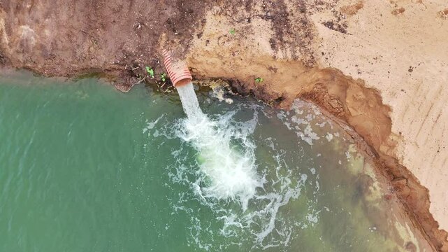 A pipe is being used to drain water from a body of water. The water is green and the pipe is red