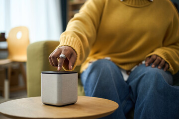 Close-up of woman interacting with smart speaker while sitting in cozy room engaging device on...