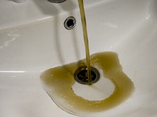 Rusty or dirty water flowing from a tap into a white bathtub or sink
