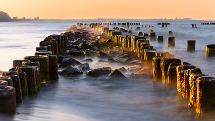 Obraz premium breakwater on the Baltic coast illuminated by the sun at golden hour.